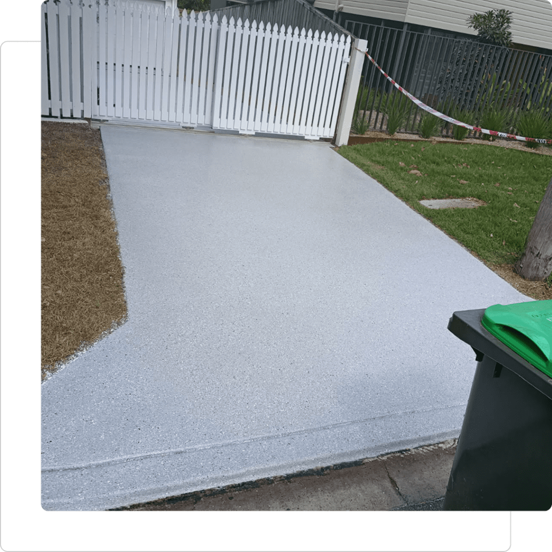 Freshly paved driveway beside white picket fence.